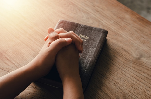 Foto menina sentada e orando pelas bênçãos de deus com a bíblia de mãos postas em oração bíblica, espiritual e religiosa, comunique-se, converse com deus. amor e perdão