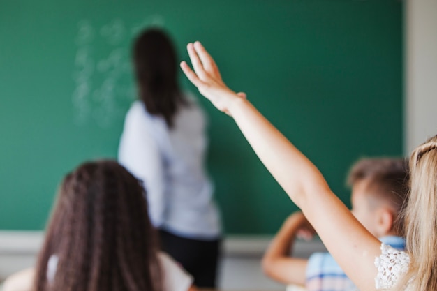 Foto menina sentada em sala de aula levantando mão