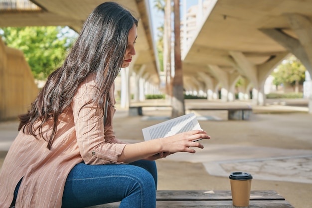 Menina sentada em um banco no parque lendo um livro