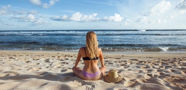 Menina sentada na areia vista traseira e olhando para o panorama do banner do oceano