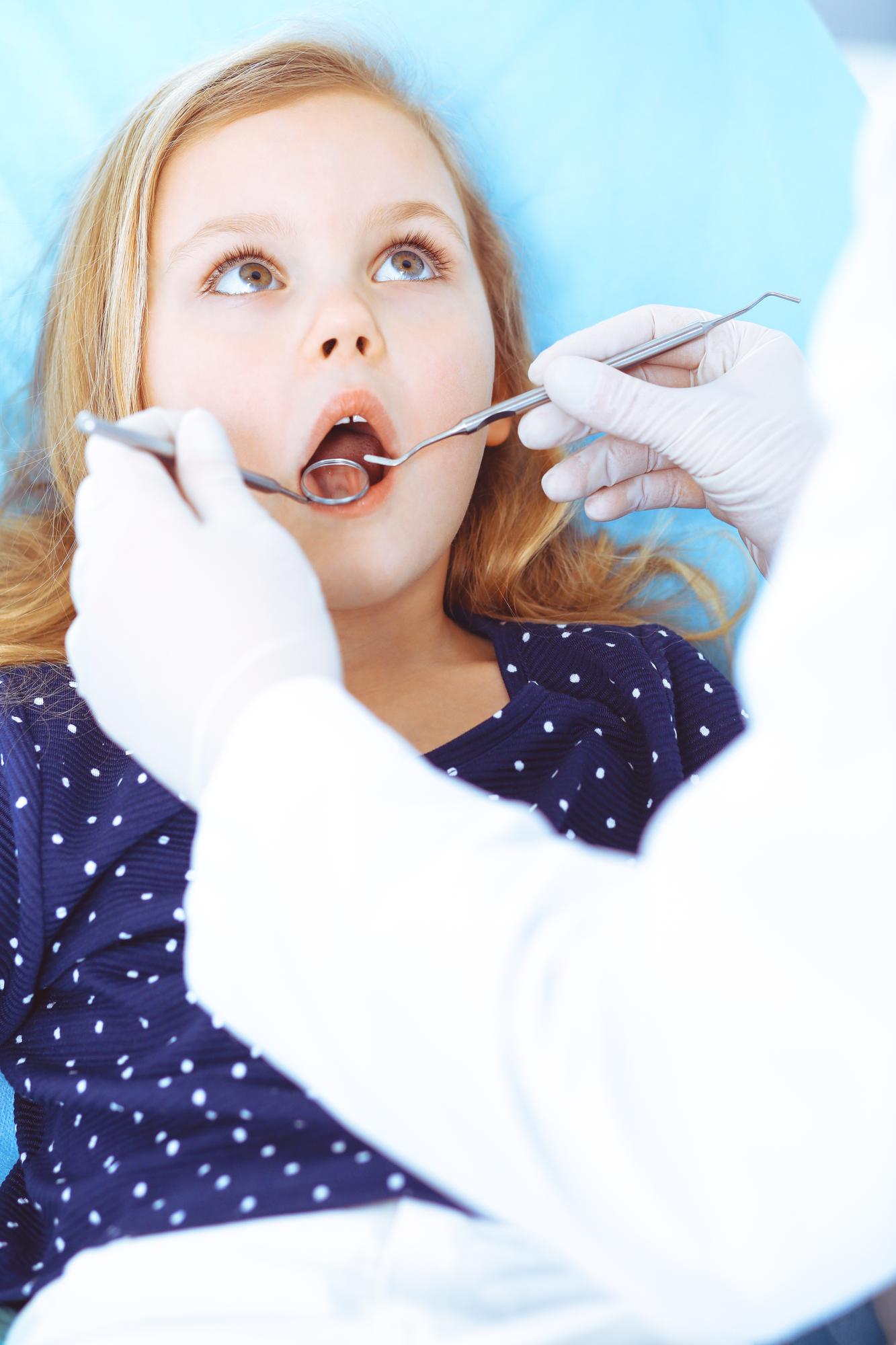 Menina sentada na cadeira odontológica com a boca aberta durante o check-up oral enquanto médico. Visitando o consultório do dentista. Conceito de medicina. Foto tonificada.