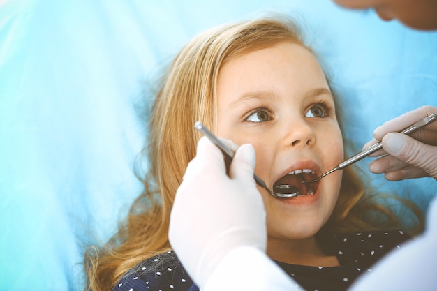 Menina sentada na cadeira odontológica com a boca aberta durante o check-up oral enquanto médico. Visitando o consultório do dentista. Conceito de medicina. Foto tonificada.