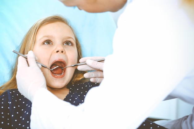 Menina sentada na cadeira odontológica com a boca aberta durante o check-up oral enquanto médico. Visitando o consultório do dentista. Conceito de medicina. Foto tonificada.