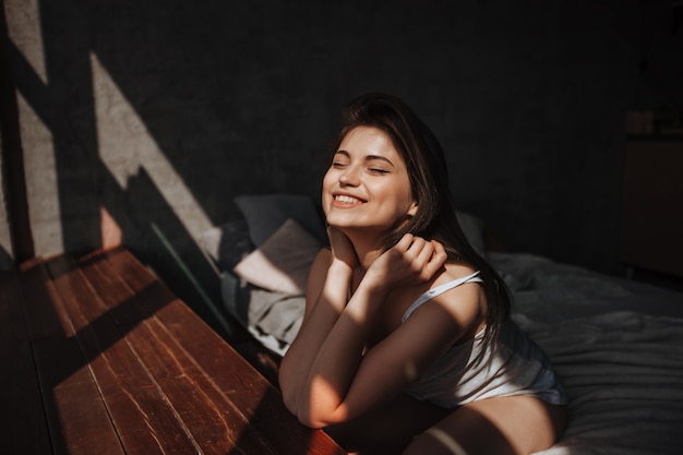 Menina sentada na cama perto da janela ao sol