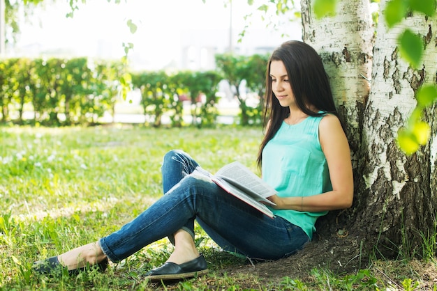 Menina sentada na grama lendo livro no verão