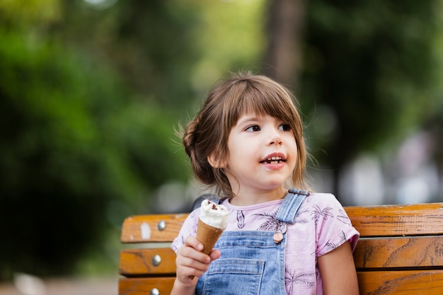 Foto menina sentada no banco enquanto come sorvete