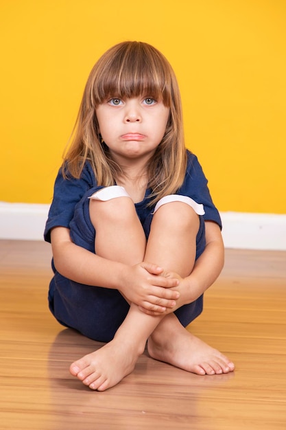 Menina sentada no chão com curativo no joelho simulando uma contusão