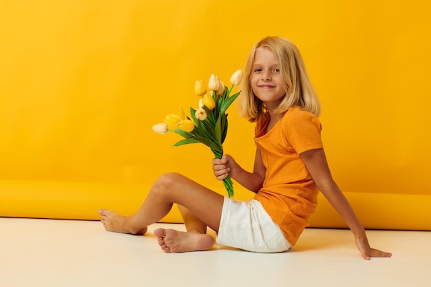 Menina sentada no chão com um buquê de flores amarelas fundo amarelo divertido