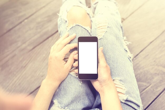 Menina sentada no chão com um celular em branco