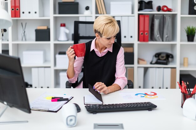 Menina sentada no escritório à mesa e tomando café.