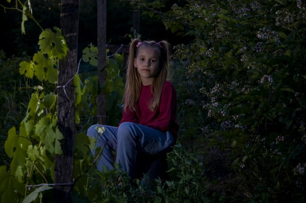 Menina sentada no jardim à noite perto das uvas