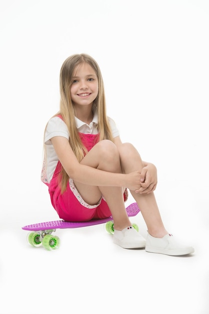 Menina sentada no skate isolado no branco Sorriso de patinador infantil com longboard Garoto de skate em macacão rosa Atividade esportiva e energia Infância e jogos ativos Beleza no skate