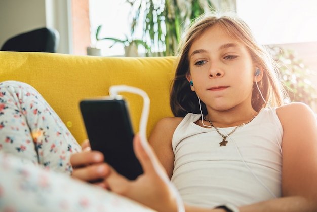 Menina sentada no sofá e usando telefone inteligente