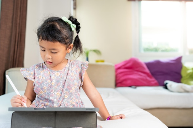 Menina sentada no sofá usando tablet em casa conceito de aprendizagem em casa