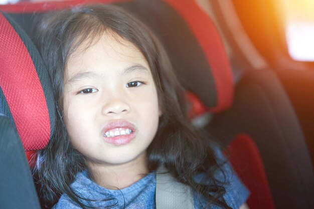 Menina sente-se no assento do carro com cinto na proteção de segurança do transporte