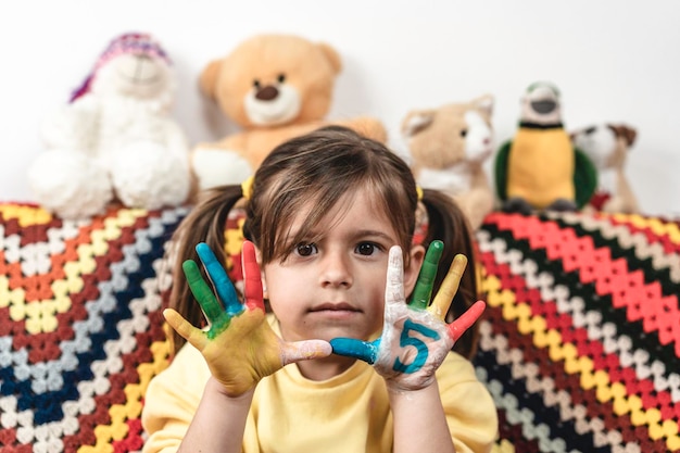 Menina séria com o número cinco pintado na mão olhando a câmera na sala de estar menina pintando as mãos com carinhas e números o número cinco e o conceito de infância