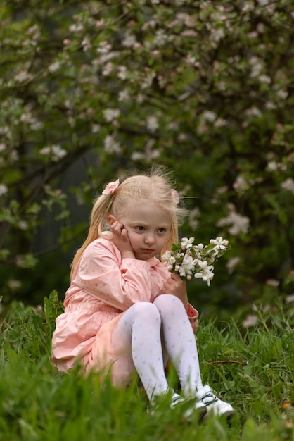 Foto menina séria ou zangada sentada no chão com flores nas mãos ressentimento infantil quadro vertical