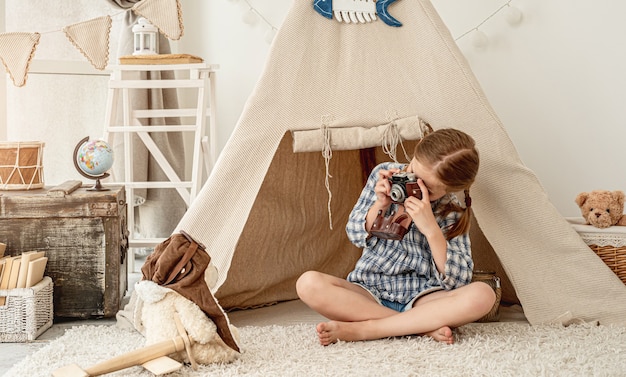 Menina simpática fotografando ursinho de pelúcia em cabana instalada na sala de jogos