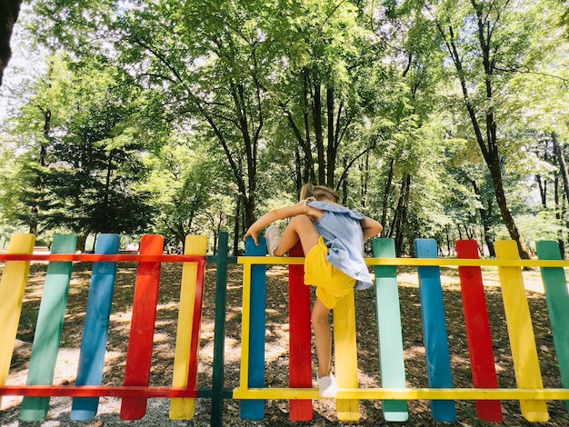 Menina sobe sobre uma cerca colorida no playground