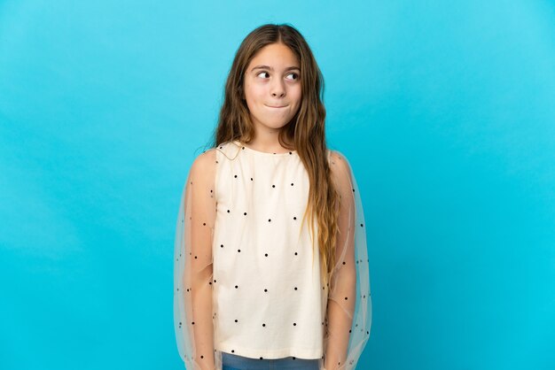 Menina sobre fundo azul isolado tendo dúvidas enquanto olha para cima