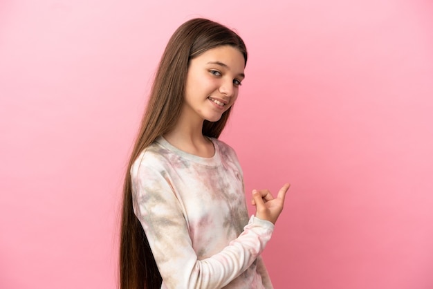 Menina sobre fundo rosa isolado apontando para trás