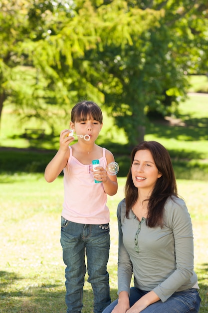 Menina soprando bolhas com sua mãe no parque