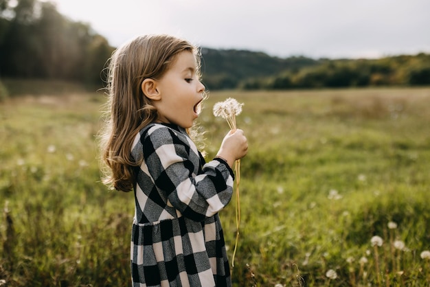 Foto menina soprando dente-de-leão vestindo um vestido em um dia de verão em um campo