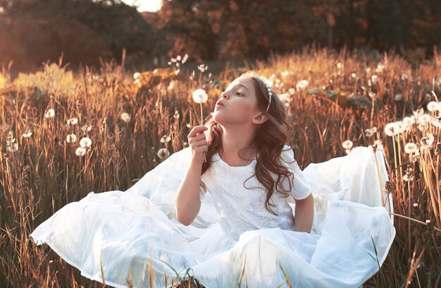 Menina soprando sementes de um dente-de-leão de flores na tarde de outono