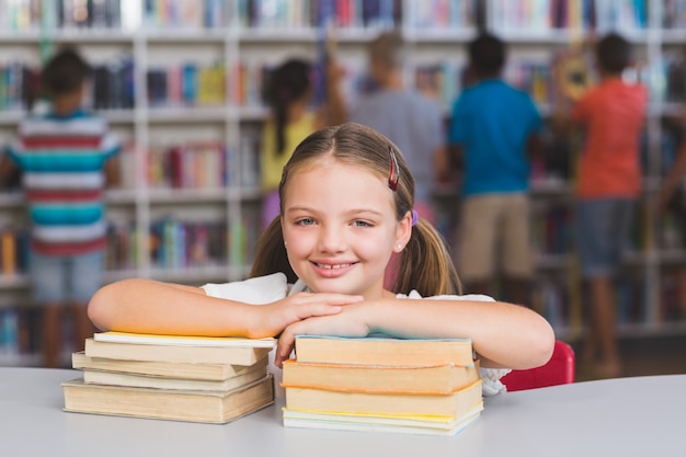 Menina sorridente, apoiando-se na pilha de livros na biblioteca