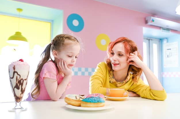 Menina sorridente, apreciando seu almoço pouco saudável com a mãe. Fazer dieta, comer, estilo de vida