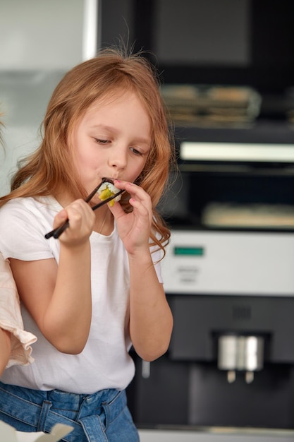 Menina sorridente bonitinha com sushi em fundo branco Menina criança comendo sushi e rolos conceito comercial