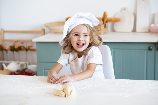 Menina sorridente, brincando com massa para biscoitos na cozinha