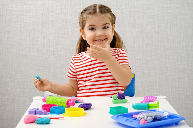 Menina sorridente brincando com massinha de plasticina colorida na mesa branca jogos educativos em casa conceito de infância feliz