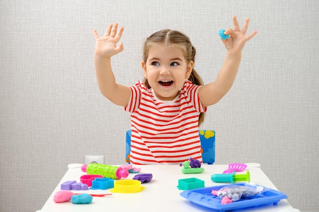 Menina sorridente brincando com plasticina colorida, argila, massinha na mesa branca, jogos educativos em casa,