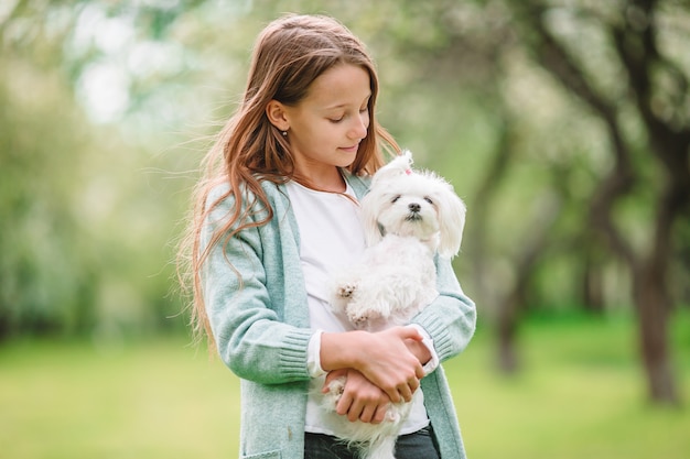 Menina sorridente brincando e abraçando cachorrinho no parque