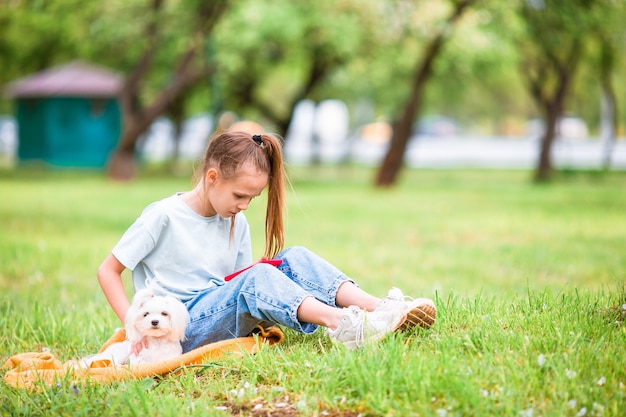 Menina sorridente brincando e abraçando o cachorrinho no parque