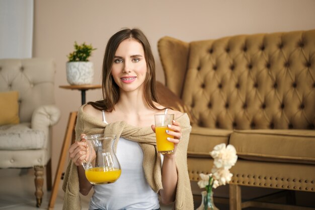 Menina sorridente com aparelho nos braços segurando um copo e uma jarra com suco nas mãos