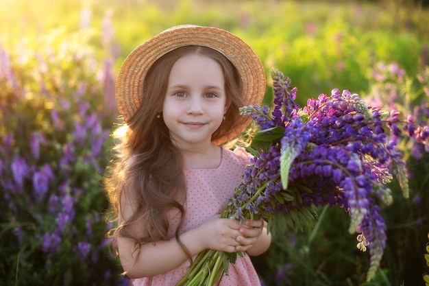 Menina sorridente com buquê de tremoços uma menina criança em um campo de tremoços em um prado de verão