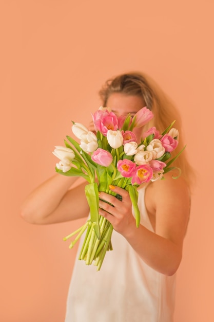 Menina sorridente com cabelo loiro e flores tulipas nas mãos. Linda jovem segurando um buquê de tulipas cor de rosa na primavera
