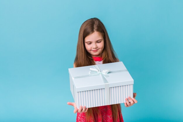 Menina sorridente com caixa de presente, parede azul.