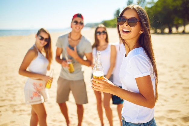 Menina sorridente com cerveja enquanto as pessoas fazem churrasco ao fundo Diversão na praia