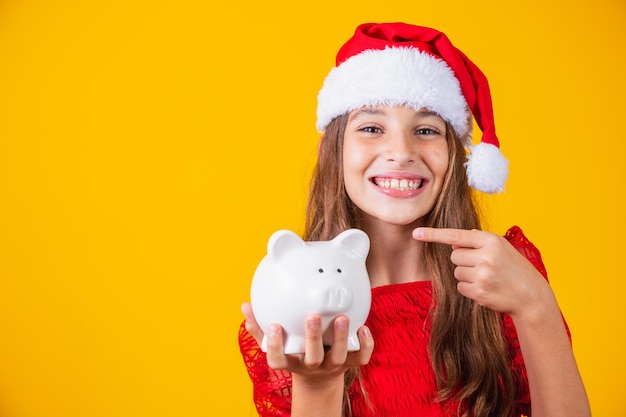 Menina sorridente com chapéu de Natal segurando o cofrinho