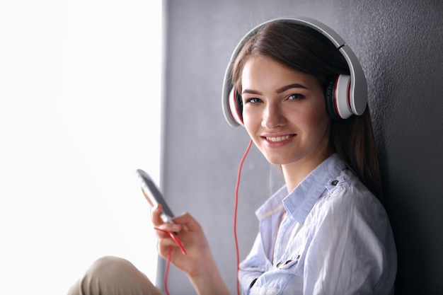 Menina sorridente com fones de ouvido sentado no chão perto da parede