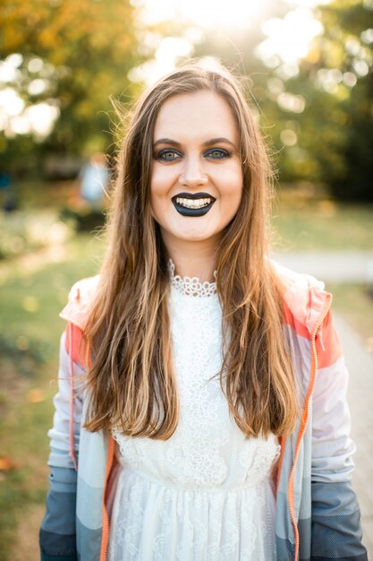 Menina sorridente com gótico compõem retrato ao ar livre no parque ensolarado