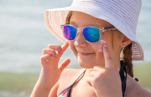 menina sorridente com manchas de chapéu protetor rosto creme na praia