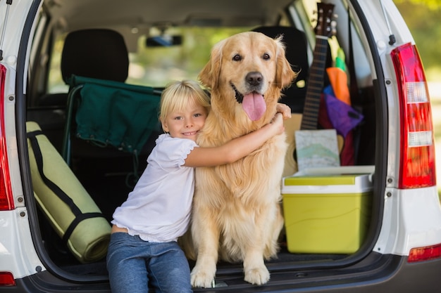 Menina sorridente com o cachorro no porta-malas do carro