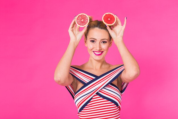 Menina sorridente com toranja cortada ao meio pela fruta na mão na parede rosa