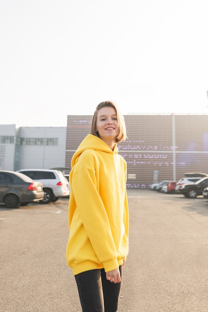 Menina sorridente com um capuz amarelo no estacionamento