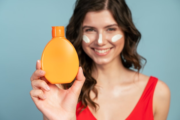 Menina sorridente com um frasco laranja de protetor solar no fundo desfocado