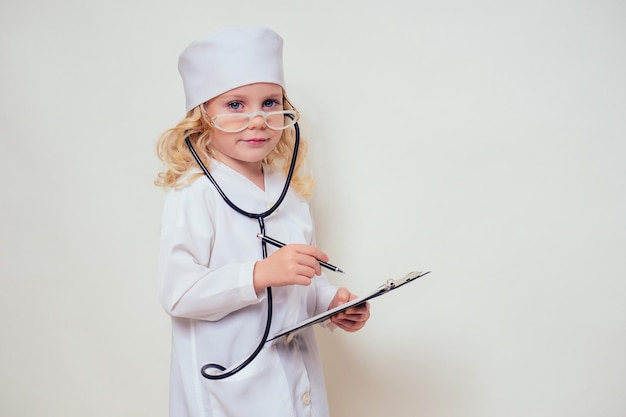 Menina sorridente com uniforme de médico com estetoscópio de ferramentas médicas escrevendo algo para a área de transferência no fundo branco no espaço de cópia do estúdio.